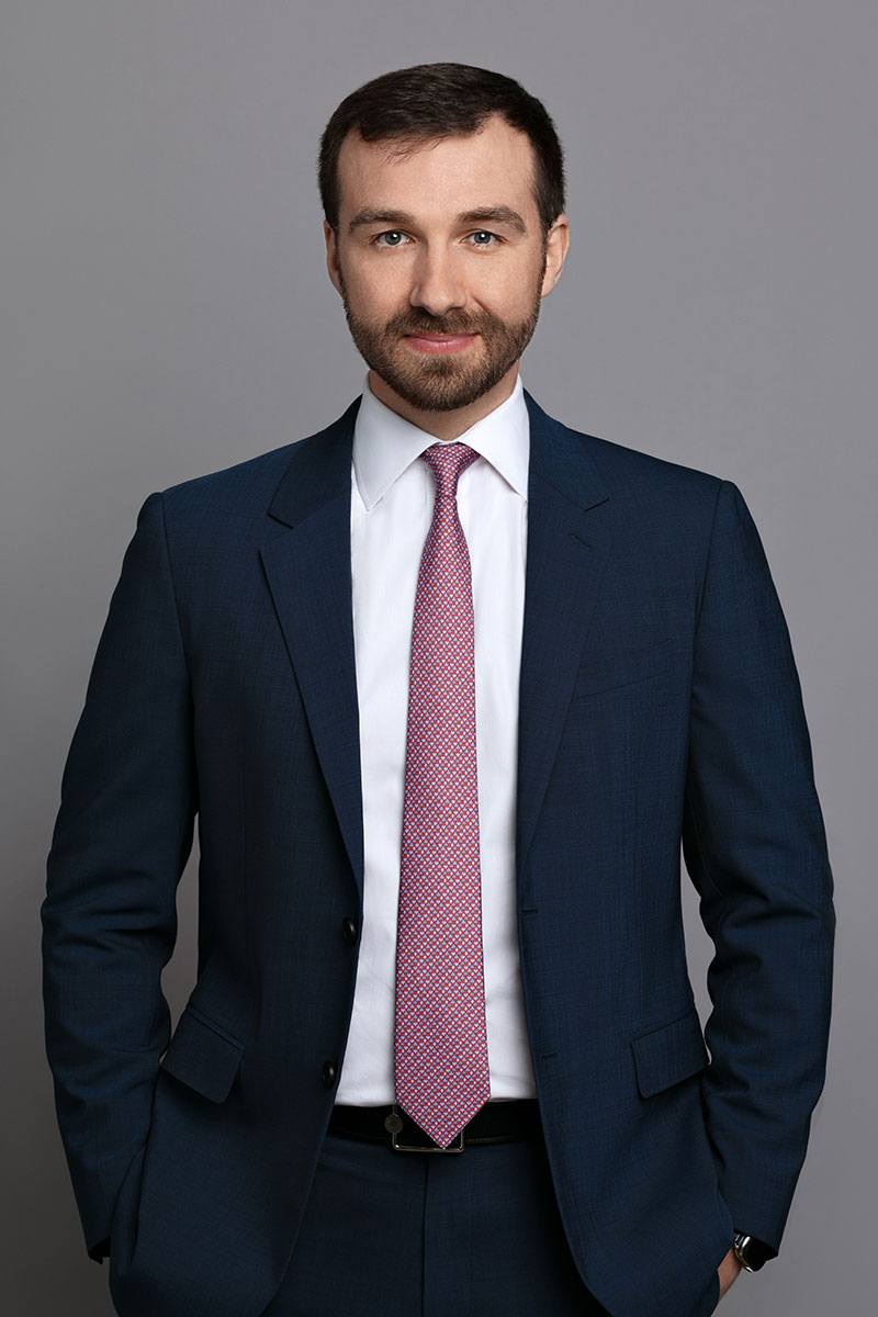 smiling man with short brown hair and beard wearing navy suit and pink tie with short brown hair