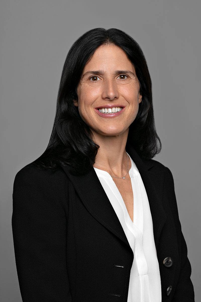 smiling woman with shoulder length black hair wearing a white button shirt on black jacket